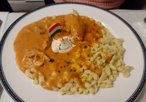 A plate of chicken in creamy sauce with a dollop of sour cream, garnished with a small flag, served with dumplings.