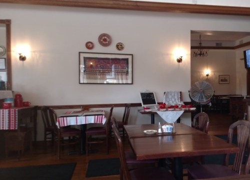 Cozy restaurant interior with wooden tables, decorative plates on the wall, and a fan in the corner.