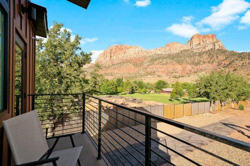 A balcony view overlooking a scenic landscape with red rock formations and green fields under a blue sky.