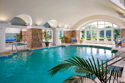 Indoor swimming pool with stone accents, lounge chairs, and large windows overlooking greenery.