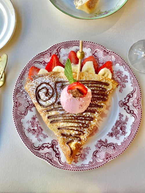 A slice of dessert topped with chocolate drizzle, strawberries, bananas, and a scoop of pink ice cream on a decorative plate.