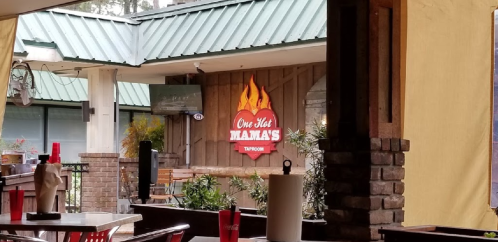 Sign for "One Hot Mamas Taproom" with a flame logo, viewed from an outdoor seating area.