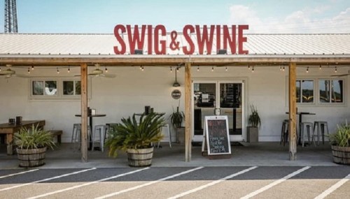 Exterior of Swig & Swine restaurant with a sign, outdoor seating, and potted plants.