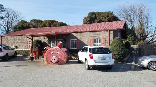 A rustic building with a red roof, featuring a large pig sculpture made of hay in the front yard.