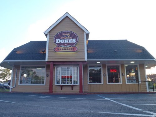A restaurant building with a sign reading "Dukes Barbecue," featuring a peaked roof and large windows.