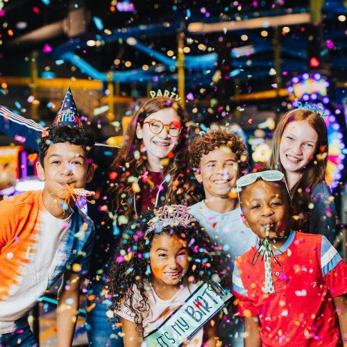 A group of cheerful children wearing party hats, celebrating with confetti and smiles at a birthday party.