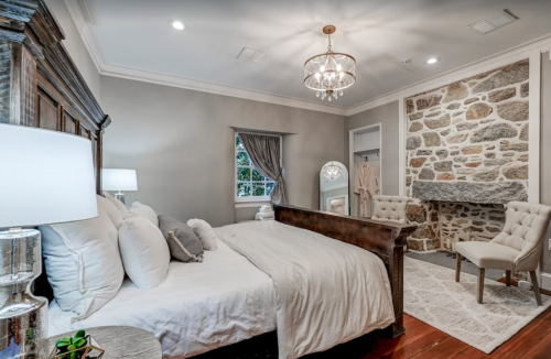 Cozy bedroom featuring a wooden bed, stone accent wall, elegant chandelier, and soft lighting.