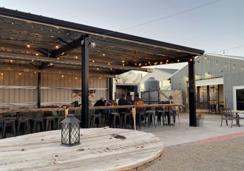 Outdoor dining area with string lights, wooden tables, and a rustic building in the background during twilight.