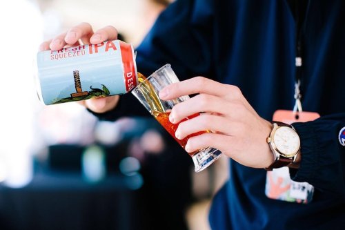 A person pours a can of Fresh Squeezed IPA into a glass, showcasing the drink's vibrant color.