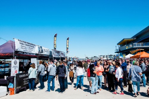 A bustling outdoor market scene with crowds enjoying food stalls under a clear blue sky.