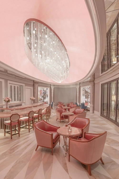 Elegant lounge with pink ceiling, crystal chandelier, and stylish seating arrangements. Soft lighting creates a cozy atmosphere.