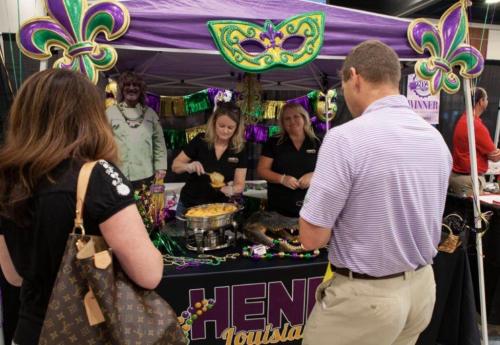 A festive booth with purple and green decorations, featuring two women serving food to attendees at an event.