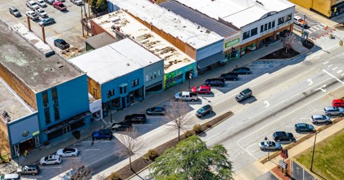 Aerial view of Main Street in Walhalla, a small town in SC, with several colorful, brick storefronts, parked cars, and a busy road.
