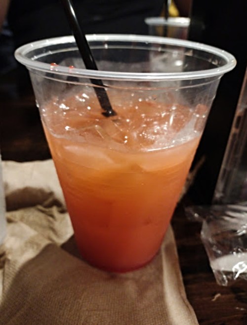 A clear plastic cup filled with a red drink and ice, with a black straw, sitting on a napkin.