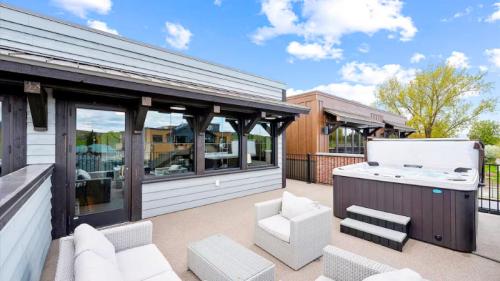 A rooftop terrace featuring a hot tub and outdoor seating with a view of nearby buildings and blue sky.