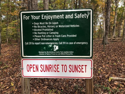Sign in a wooded area outlining park rules: dogs on leash, no alcohol, no hunting, and littering prohibited.