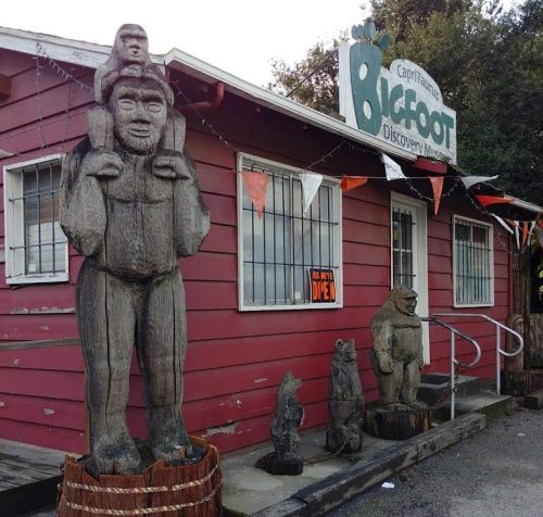 A red building with a sign reading "Bigfoot Discovery Museum" and wooden Bigfoot sculptures outside.