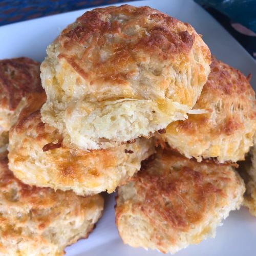 Golden, flaky biscuits stacked on a plate, with a bite taken out of one, showcasing a soft, fluffy interior.