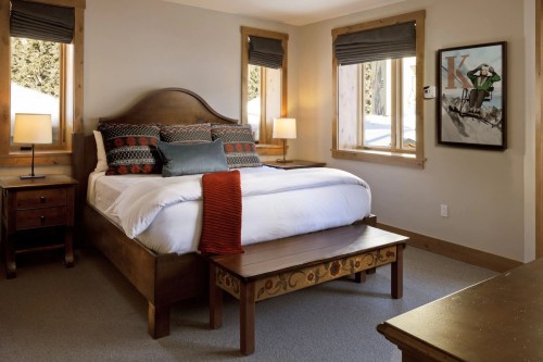 Cozy bedroom with a large bed, decorative pillows, wooden furniture, and windows letting in natural light.