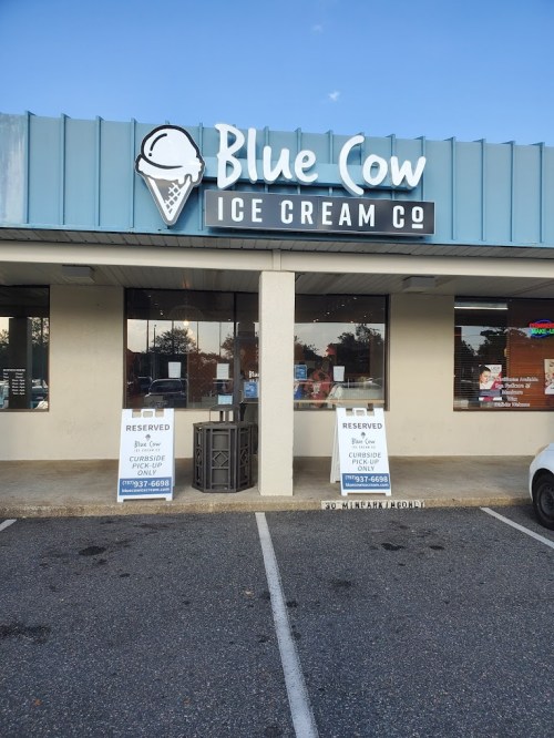Exterior of Blue Cow Ice Cream Co. with two reserved signs in front and a clear blue sky above.