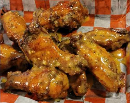 A close-up of golden-brown chicken wings coated in a sticky sauce, served on a checkered paper.