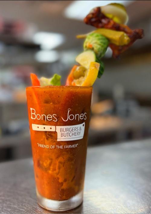 A vibrant Bloody Mary garnished with vegetables and a crispy bacon strip, served in a glass from Bones Jones Burgers & Butchery.