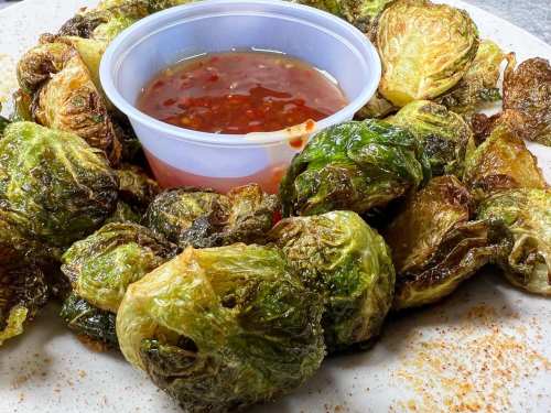 A plate of crispy Brussels sprouts surrounding a small container of sweet chili sauce.