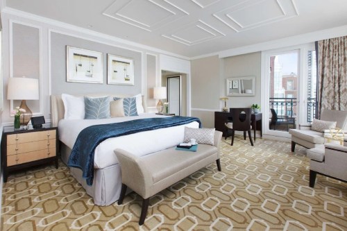 Luxurious hotel room featuring a king bed, elegant decor, seating area, and large windows with city views.