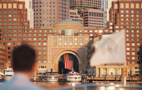 A view of a large building with an American flag, seen from a boat on the water, with a person in the foreground.