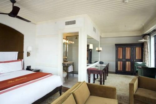 A stylish hotel room featuring a bed, seating area, desk, and an en-suite bathroom with modern decor.