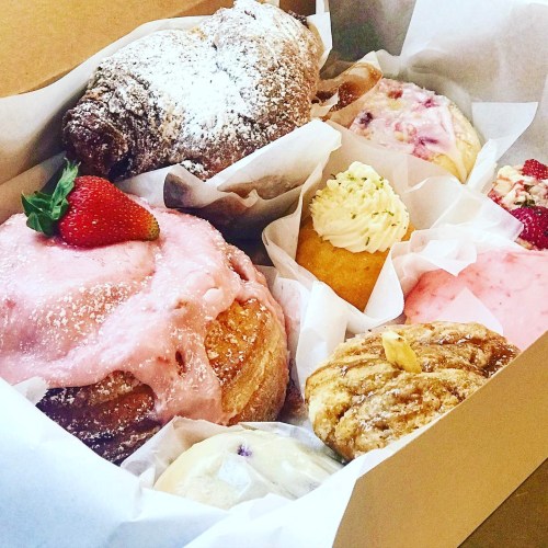 A box filled with assorted pastries, including a croissant, sweet rolls, and cupcakes, garnished with strawberries.