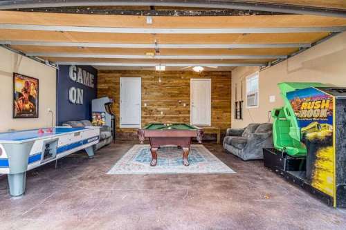 A game room in a garage featuring a pool table, arcade machine, air hockey table, and cozy seating.