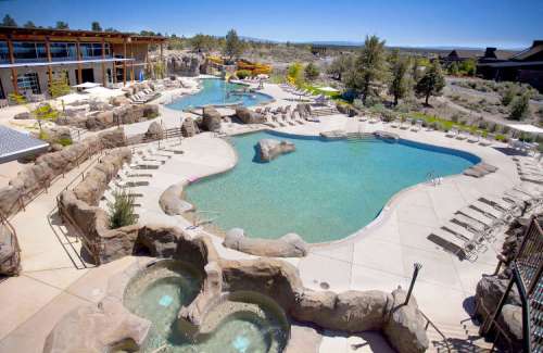 A scenic resort pool area with rock formations, lounge chairs, and clear blue water under a sunny sky.