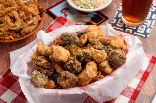 A basket of crispy fried vegetables, including okra and mushrooms, served with coleslaw and a drink in the background.