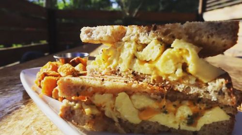 A close-up of a sandwich filled with scrambled eggs and cheese, served with a side of crispy potatoes.