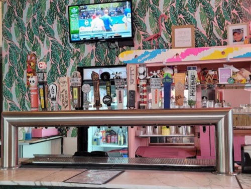 A colorful bar with various beer taps, a marble countertop, and a TV showing a sports event in a tropical-themed setting.