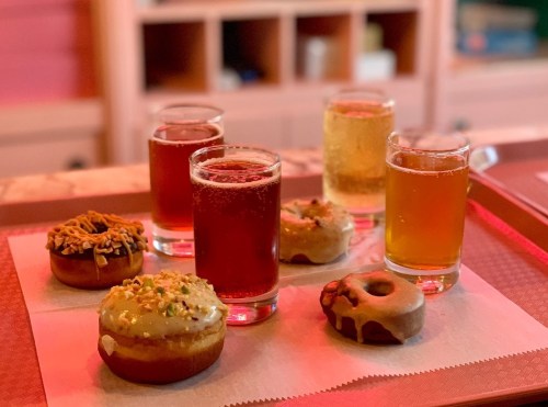 A colorful assortment of donuts and drinks on a tray, featuring two types of donuts and three glasses of beverages.