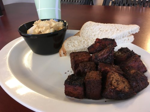 A plate with cubed, smoked meat, a side of creamy dip, and two slices of bread on a wooden table.