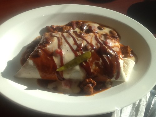 A plate of enchiladas topped with sauce, cheese, and a green chili, served on a white dish.