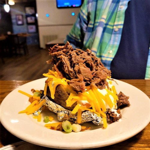 A loaded baked potato topped with shredded beef, cheese, sour cream, and green onions on a white plate.