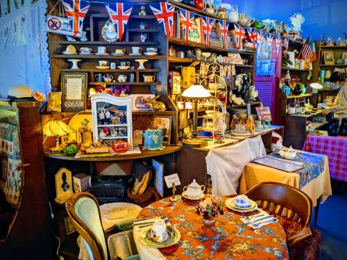 A cozy vintage shop display with teacups, memorabilia, and decorative items, featuring British flags and a charming dining setup.