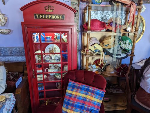 A vintage red telephone booth display with shelves of hats and decorative items in a cozy setting.