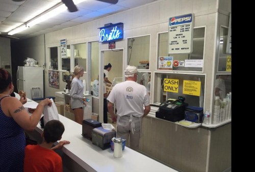 A busy diner counter with customers ordering, a cashier, and a sign that says "Cash Only" in a retro setting.