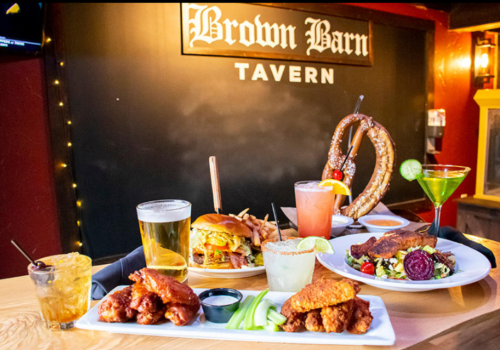A table spread featuring burgers, wings, pretzels, cocktails, and beers at Brown Barn Tavern.