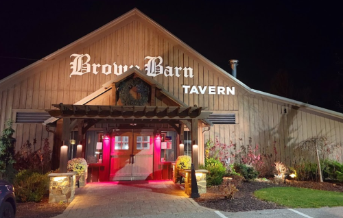 Exterior of Brow Barn Tavern at night, featuring a wooden facade and illuminated entrance with decorative plants.