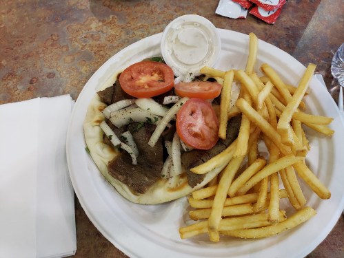 A plate with pita bread filled with sliced meat, tomatoes, and onions, accompanied by a side of French fries and dipping sauce.