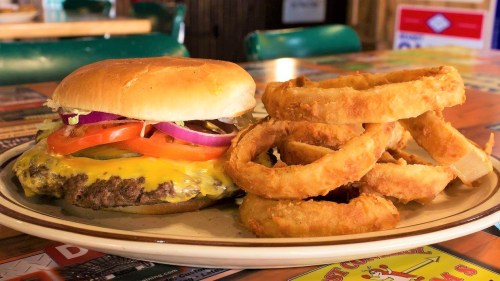A juicy cheeseburger with lettuce, tomato, and onion, served with a side of crispy onion rings on a plate.