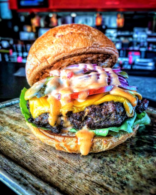A juicy cheeseburger with lettuce, tomato, and sauce, served on a toasted bun against a blurred restaurant background.