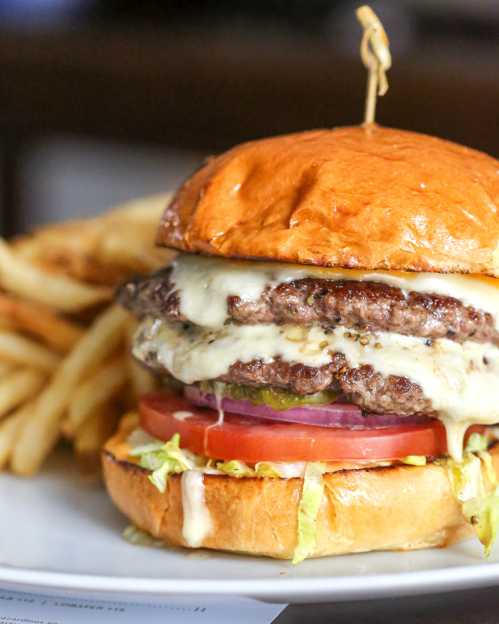 A close-up of a juicy burger with two patties, melted cheese, lettuce, tomato, and pickles, served with fries.