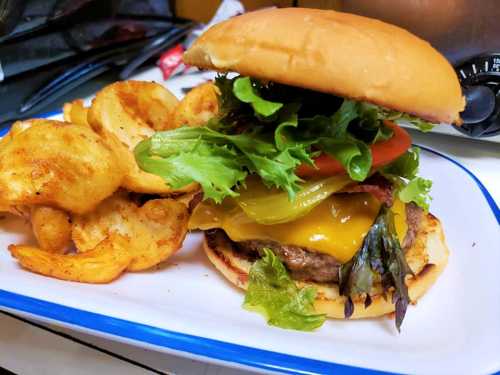 A juicy burger with lettuce, tomato, pickles, and cheese, served with crispy potato wedges on a plate.